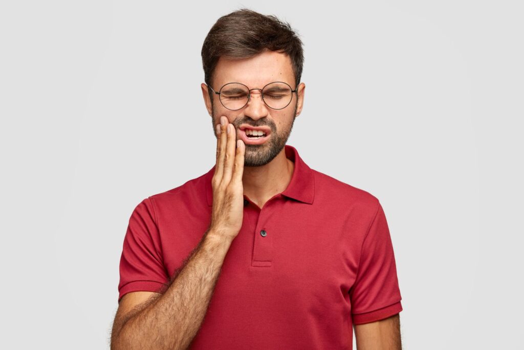 Şiddetli diş ağrısı yaşayan bireyin yanağını tutarak ağrıyı ifade ettiği klinik temalı görsel.