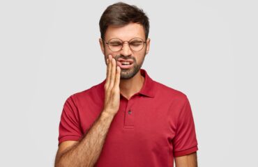 Şiddetli diş ağrısı yaşayan bireyin yanağını tutarak ağrıyı ifade ettiği klinik temalı görsel.