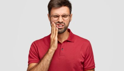 Şiddetli diş ağrısı yaşayan bireyin yanağını tutarak ağrıyı ifade ettiği klinik temalı görsel.